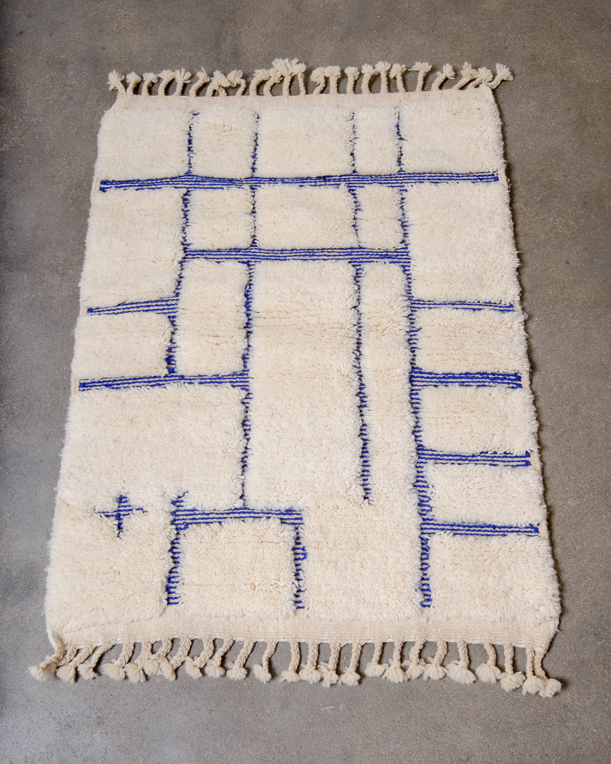 Berberlin Beniourain rug in cream and blue laying flat on concrete floor.